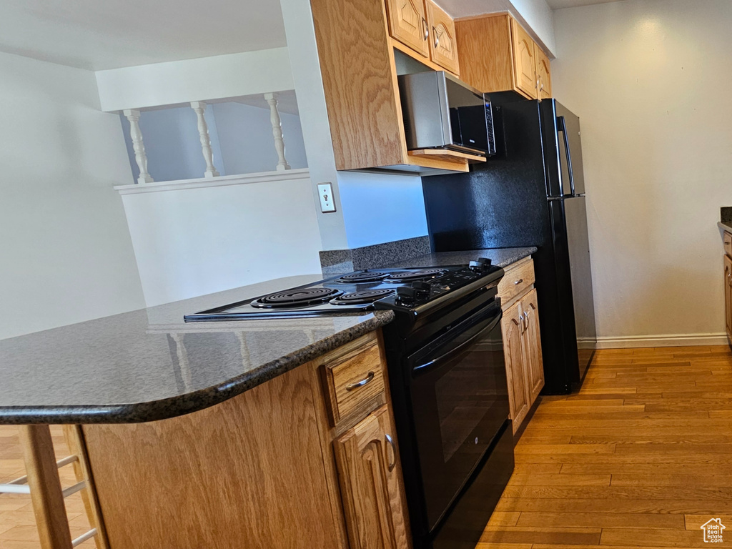 Kitchen with black appliances, wood finished floors, a peninsula, brown cabinets, and dark stone counters