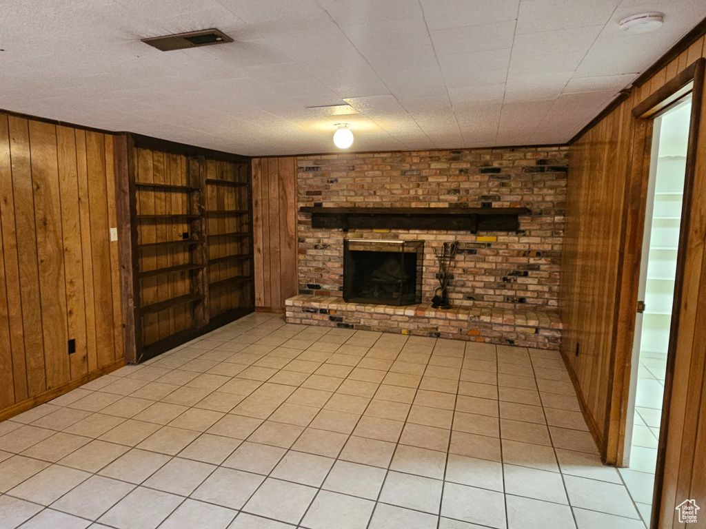 Unfurnished living room with wood walls, built in features, a brick fireplace, and light tile patterned floors
