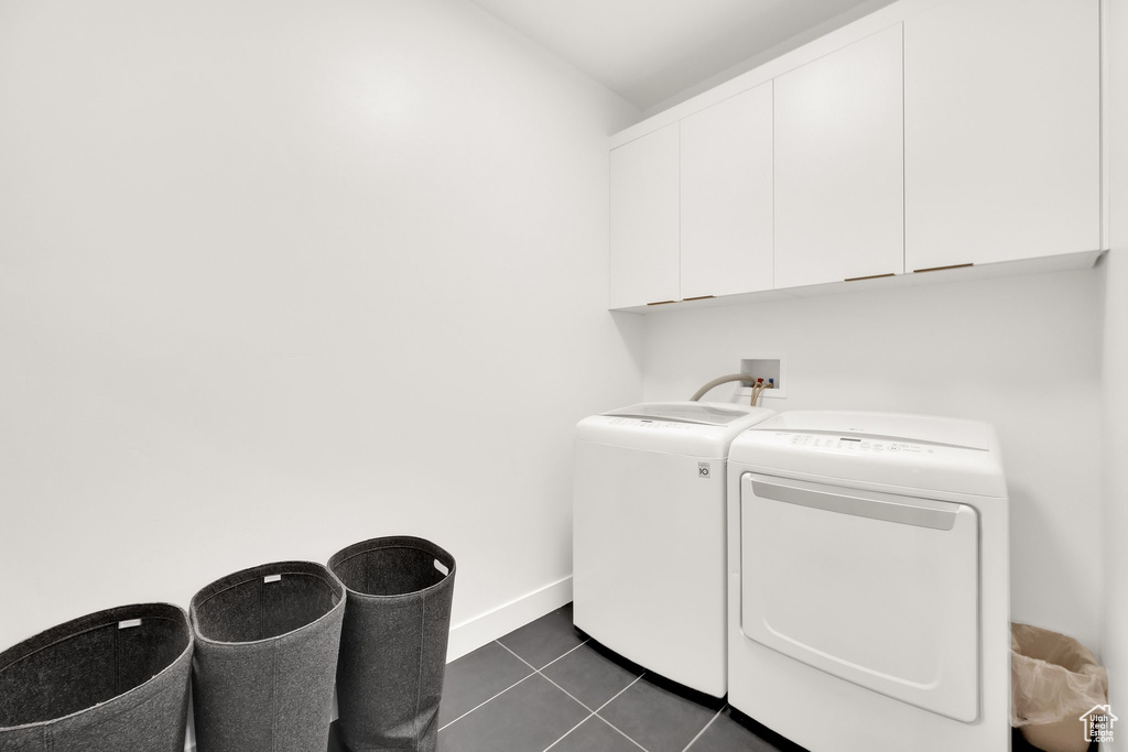 Laundry area with dark tile patterned flooring, separate washer and dryer, baseboards, and cabinet space