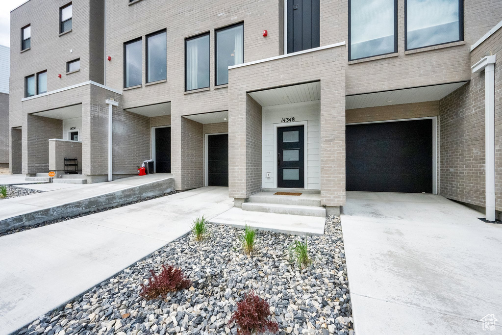 Doorway to property featuring brick siding, an attached garage, and driveway