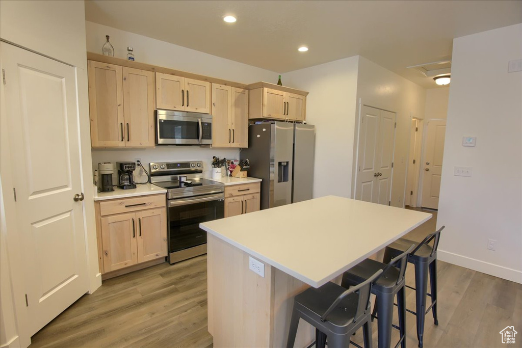 Kitchen with appliances with stainless steel finishes, a kitchen bar, light wood finished floors, and light brown cabinets