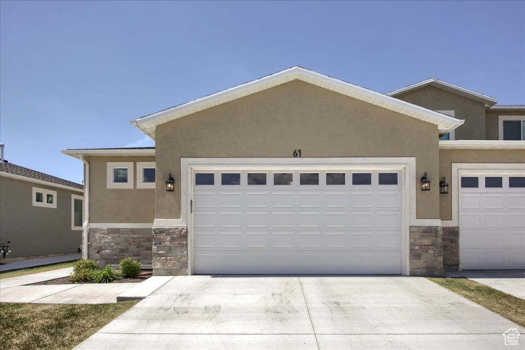 View of front facade featuring concrete driveway, stone siding, and stucco siding