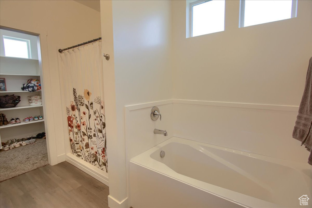 Bathroom featuring curtained shower, a wealth of natural light, a garden tub, and wood finished floors