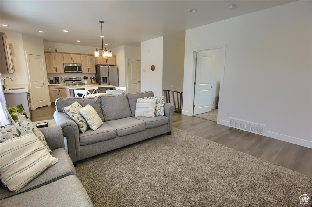 Living area with dark wood-style flooring, visible vents, baseboards, a notable chandelier, and recessed lighting