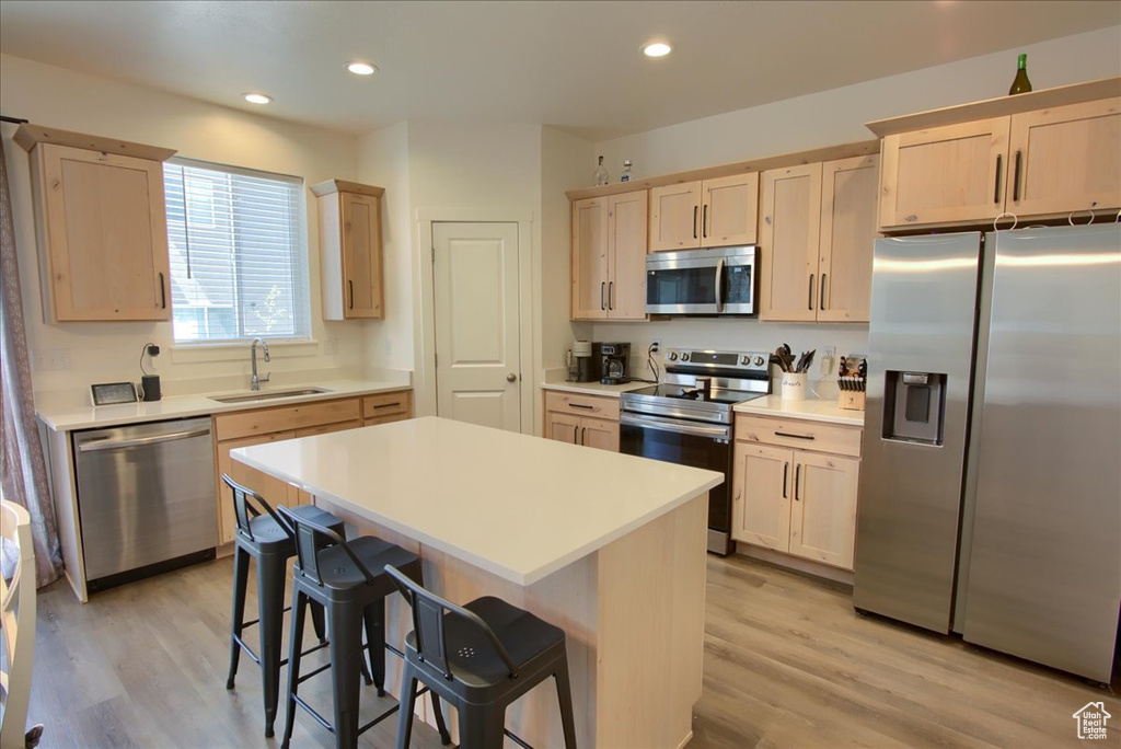 Kitchen featuring a sink, light brown cabinets, a breakfast bar area, light wood-style flooring, and stainless steel appliances