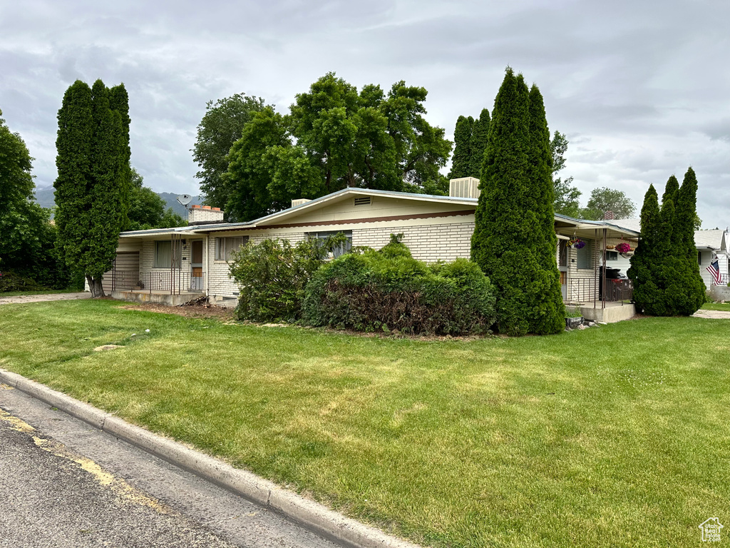 View of front facade featuring a porch, brick siding, a chimney, and a front lawn