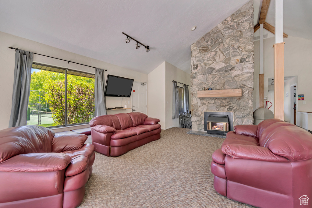 Living room featuring carpet, lofted ceiling with beams, rail lighting, and a stone fireplace