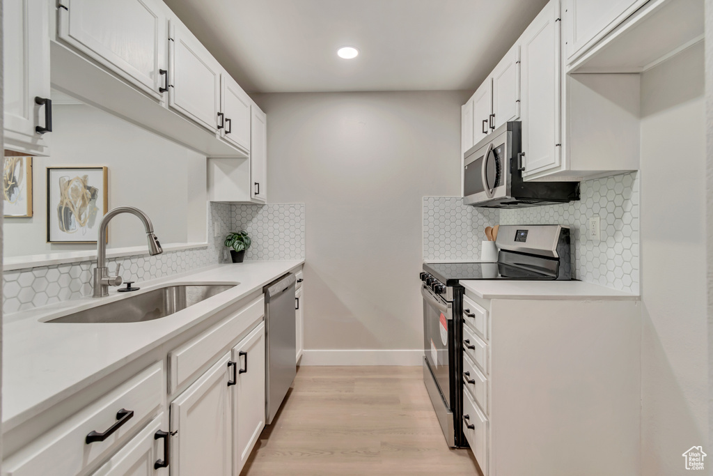 Kitchen featuring appliances with stainless steel finishes, a sink, light countertops, white cabinets, and light wood-style floors