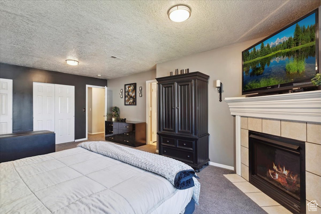 Bedroom with carpet flooring, a textured ceiling, baseboards, and a tiled fireplace