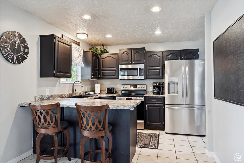 Kitchen featuring a breakfast bar area, appliances with stainless steel finishes, a sink, light countertops, and a peninsula