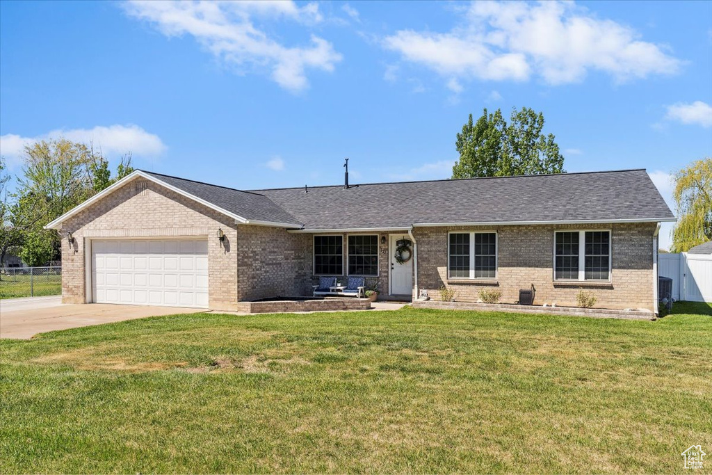 Ranch-style home with a front yard, a garage, brick siding, fence, and concrete driveway