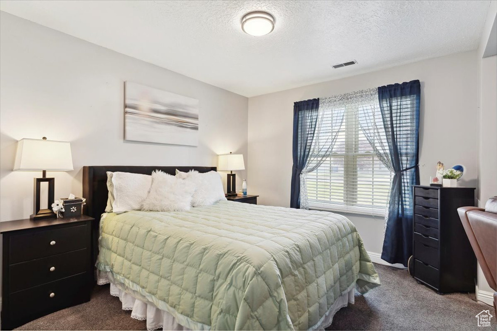 Bedroom with a textured ceiling, baseboards, visible vents, and dark carpet