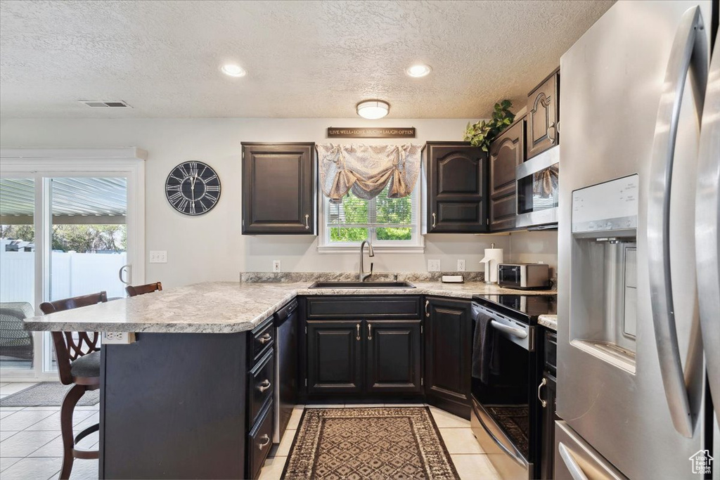 Kitchen with a sink, a textured ceiling, stainless steel appliances, a peninsula, and visible vents