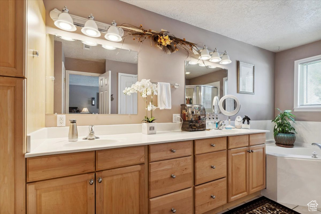 Bathroom featuring double vanity, a textured ceiling, a bath, a shower stall, and a sink