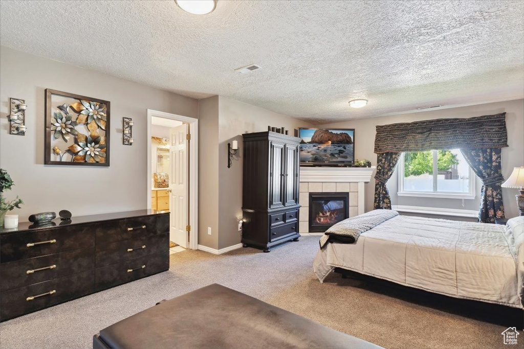 Bedroom featuring a tiled fireplace, a textured ceiling, and carpet