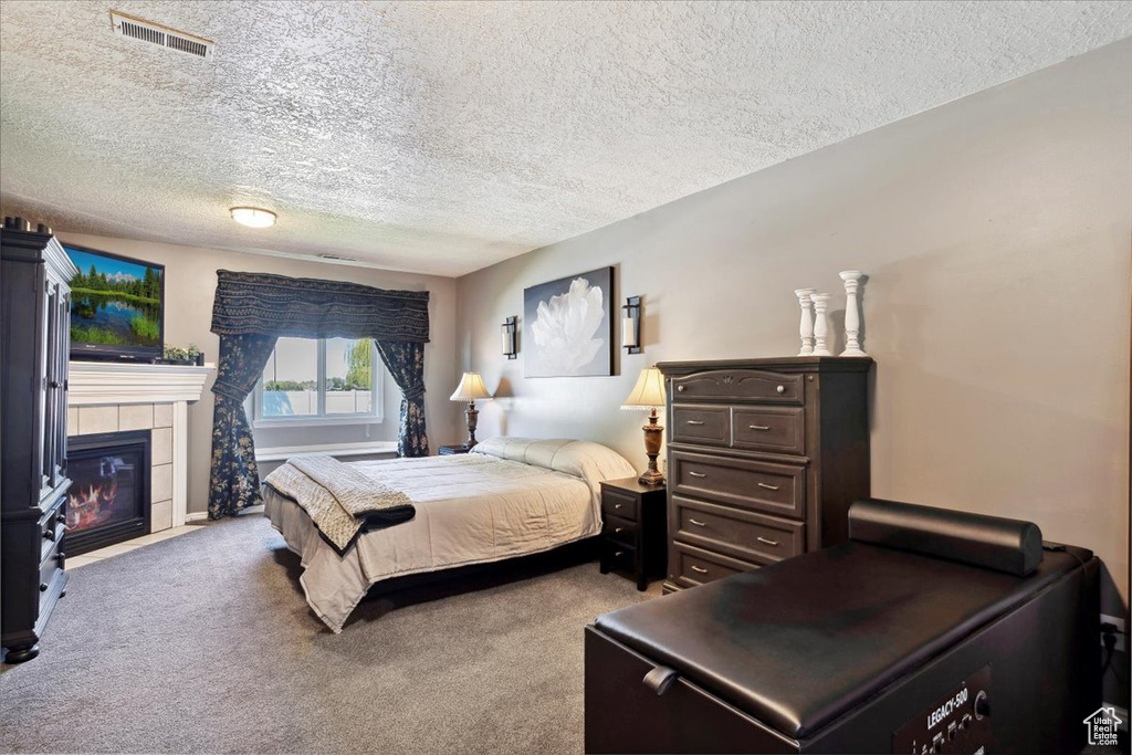 Carpeted bedroom with a textured ceiling, visible vents, and a tile fireplace