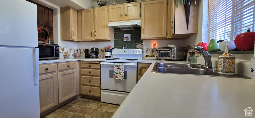 Kitchen with a toaster, white appliances, light countertops, under cabinet range hood, and a sink