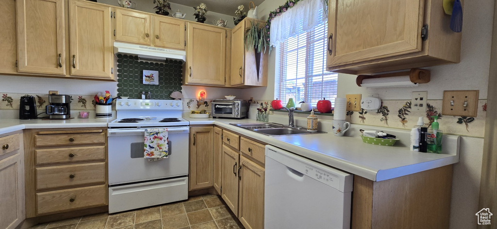 Kitchen featuring light brown cabinetry, white appliances, light countertops, under cabinet range hood, and a sink