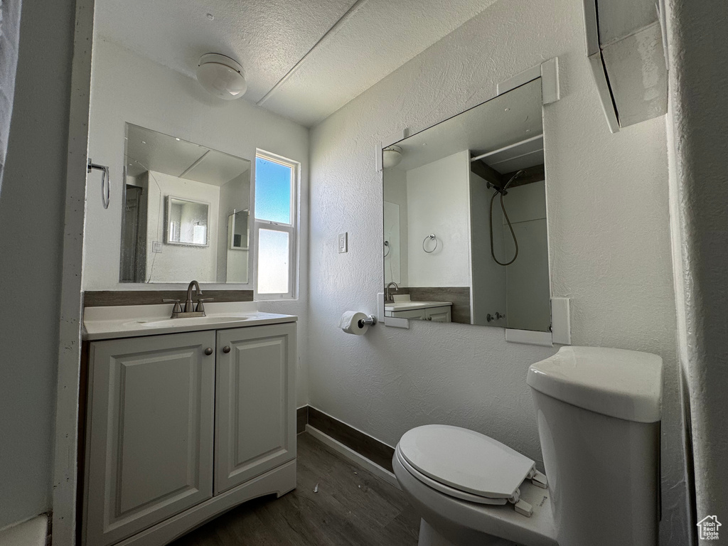 Full bath with a textured wall, wood finished floors, toilet, walk in shower, and a textured ceiling