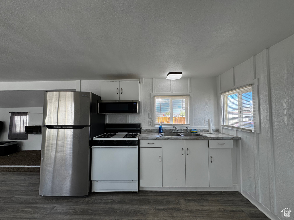 Kitchen featuring dark wood-style flooring, appliances with stainless steel finishes, a sink, a textured ceiling, and white cabinetry