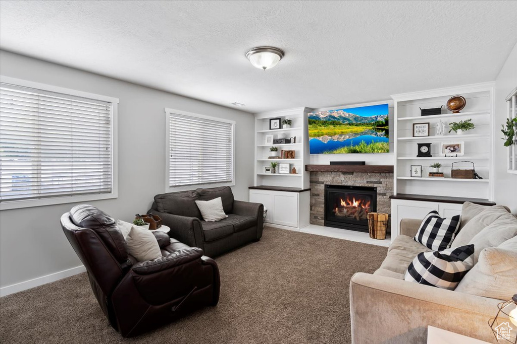 Living area featuring a textured ceiling, a stone fireplace, built in features, baseboards, and carpet flooring