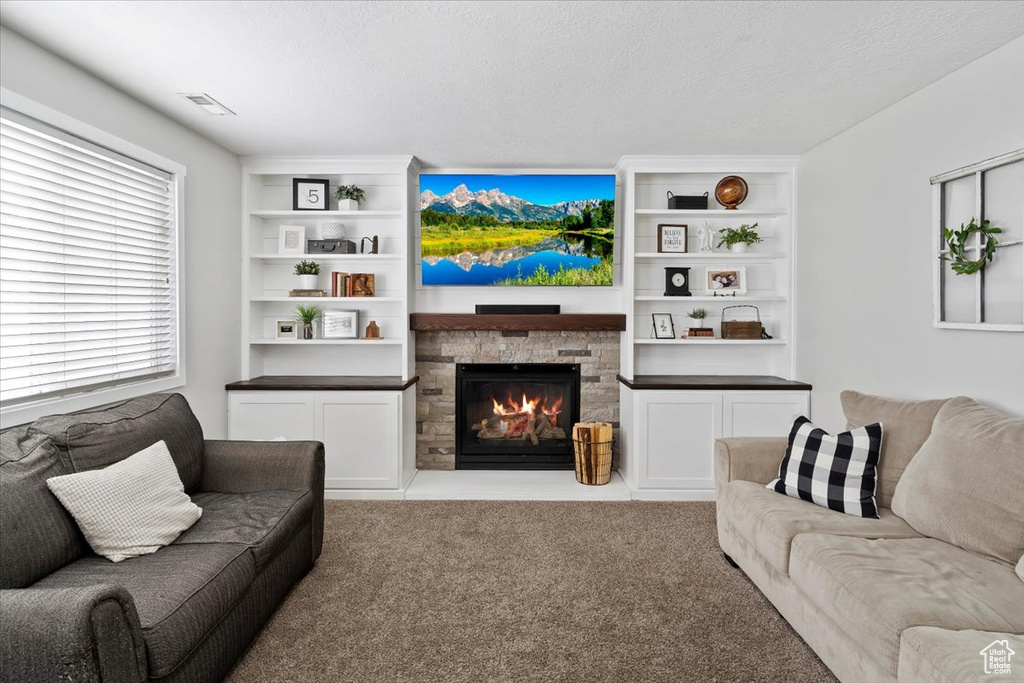 Carpeted living area featuring a textured ceiling, visible vents, and a fireplace