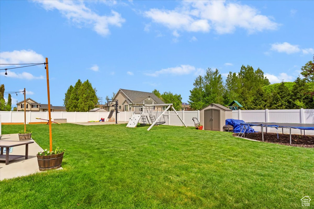 View of yard featuring a trampoline, an outdoor structure, a playground, a fenced backyard, and a storage unit
