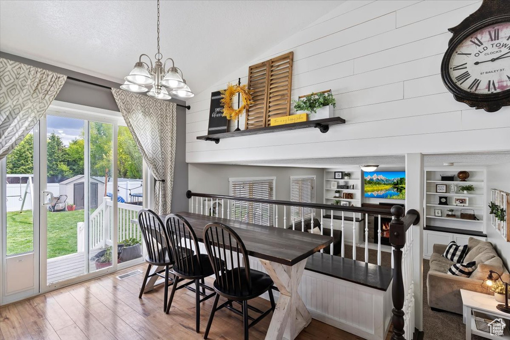 Dining space with an inviting chandelier, vaulted ceiling, wood finished floors, and visible vents