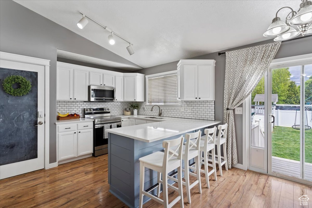 Kitchen featuring white cabinets, stainless steel appliances, a sink, and lofted ceiling