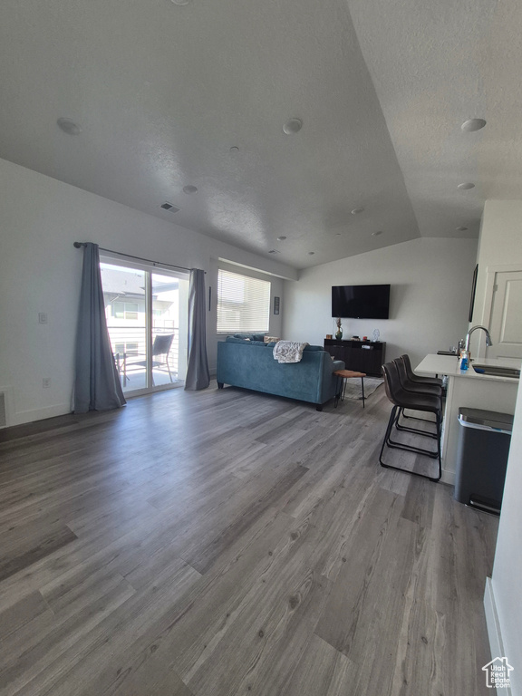 Living room with a textured ceiling, vaulted ceiling, wood finished floors, and visible vents