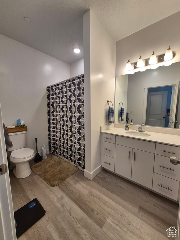 Bathroom featuring vanity, wood finished floors, toilet, baseboards, and a tile shower