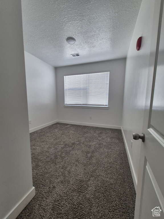 Spare room featuring baseboards, dark colored carpet, a textured ceiling, and visible vents