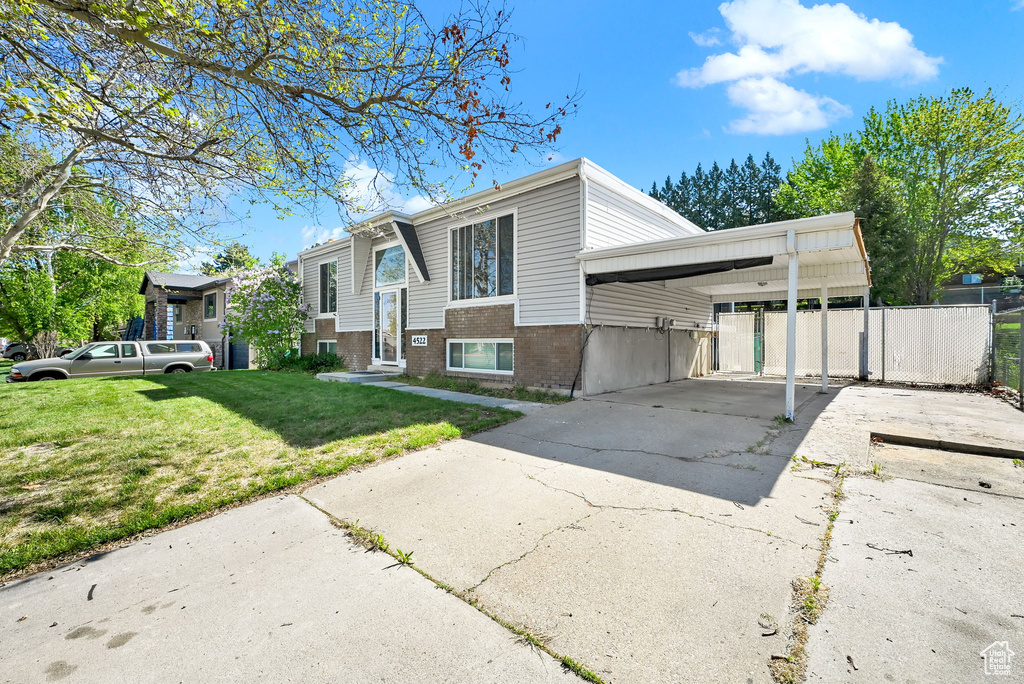 Bi-level home with fence, a front lawn, brick siding, concrete driveway, and a carport