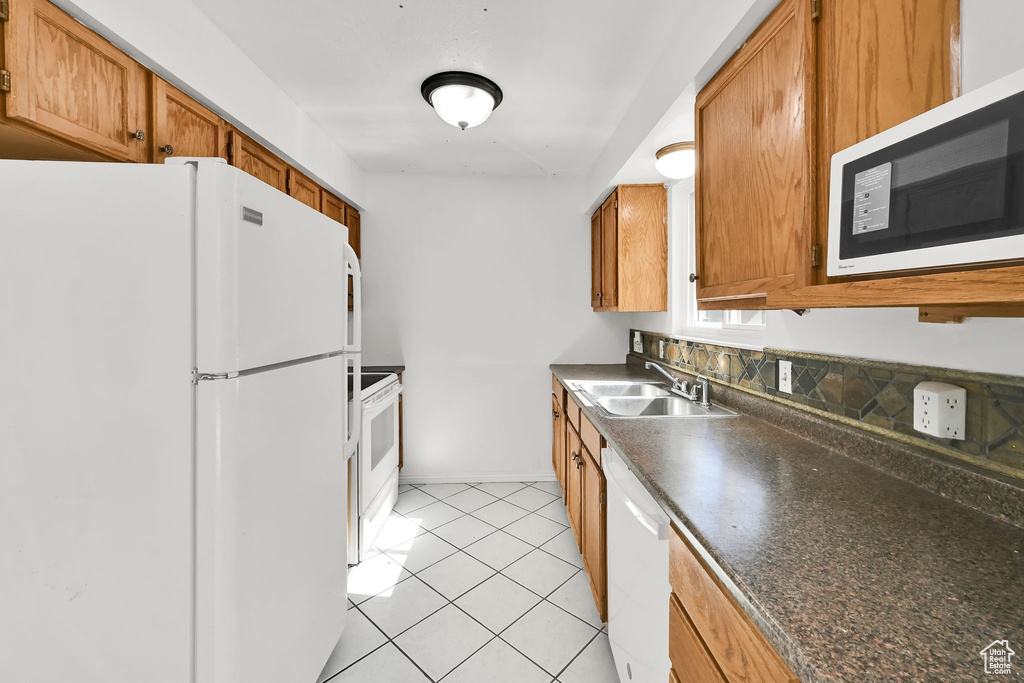 Kitchen with white appliances, dark countertops, brown cabinetry, and a sink