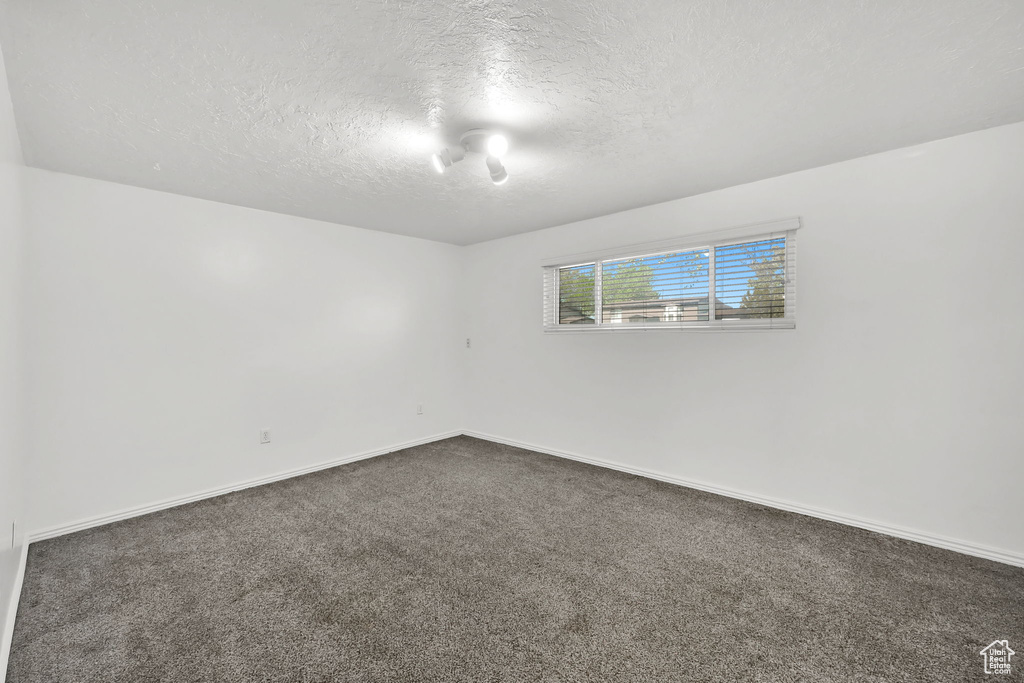 Empty room featuring baseboards, a textured ceiling, and dark carpet