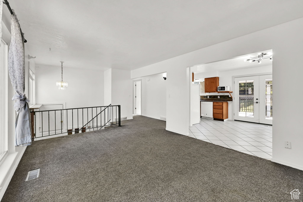 Unfurnished room with a notable chandelier, light carpet, baseboards, light tile patterned floors, and visible vents