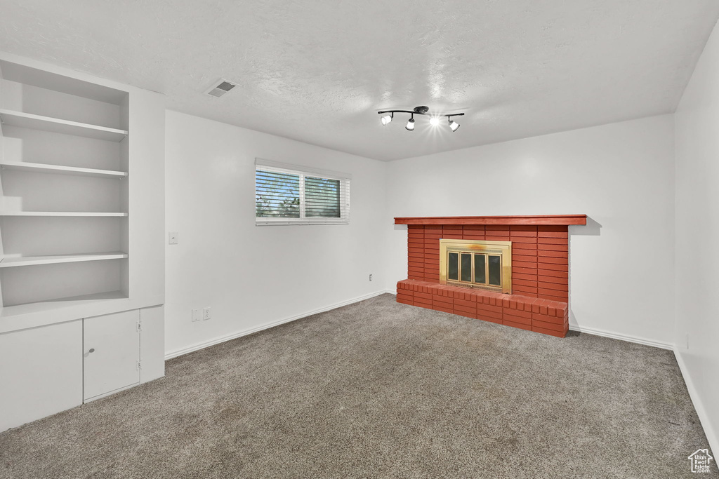 Unfurnished living room featuring baseboards, carpet, a brick fireplace, and a textured ceiling