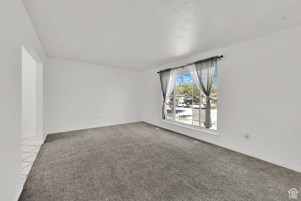 Empty room with baseboards, carpet flooring, tile patterned floors, and a textured ceiling
