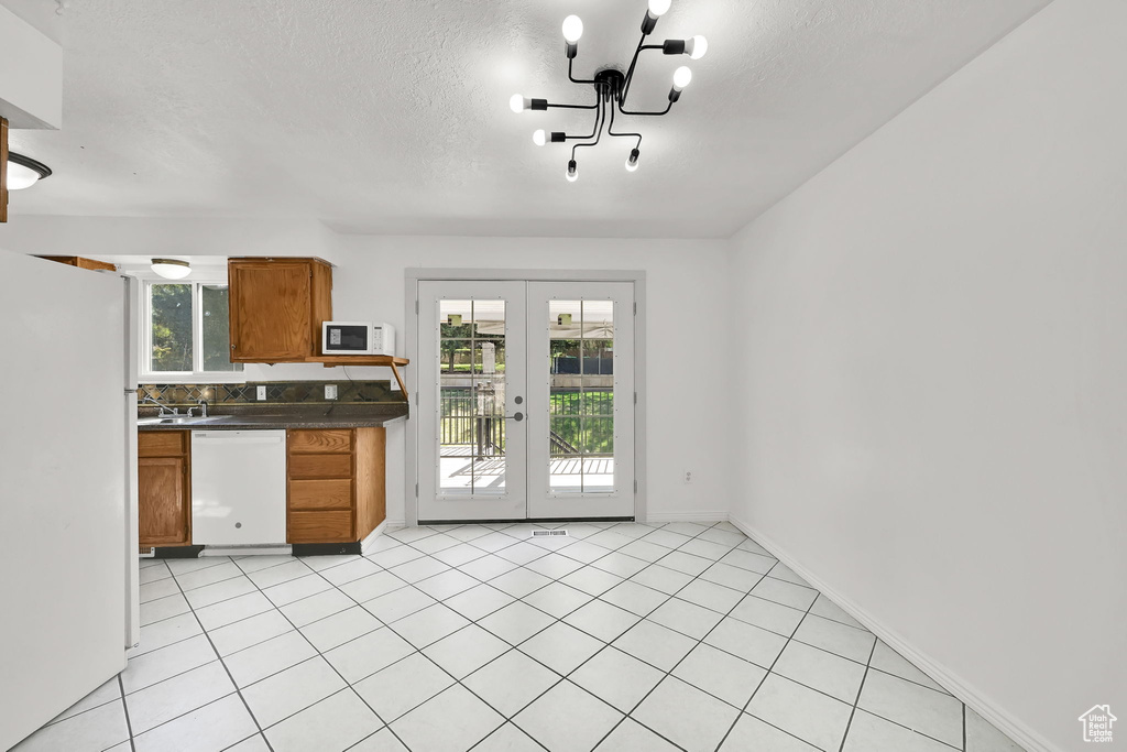 Kitchen featuring brown cabinets, dark countertops, white appliances, a textured ceiling, and french doors