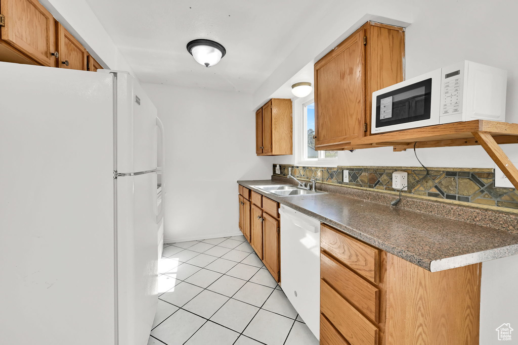 Kitchen featuring light tile patterned flooring, dark countertops, white appliances, brown cabinets, and a sink