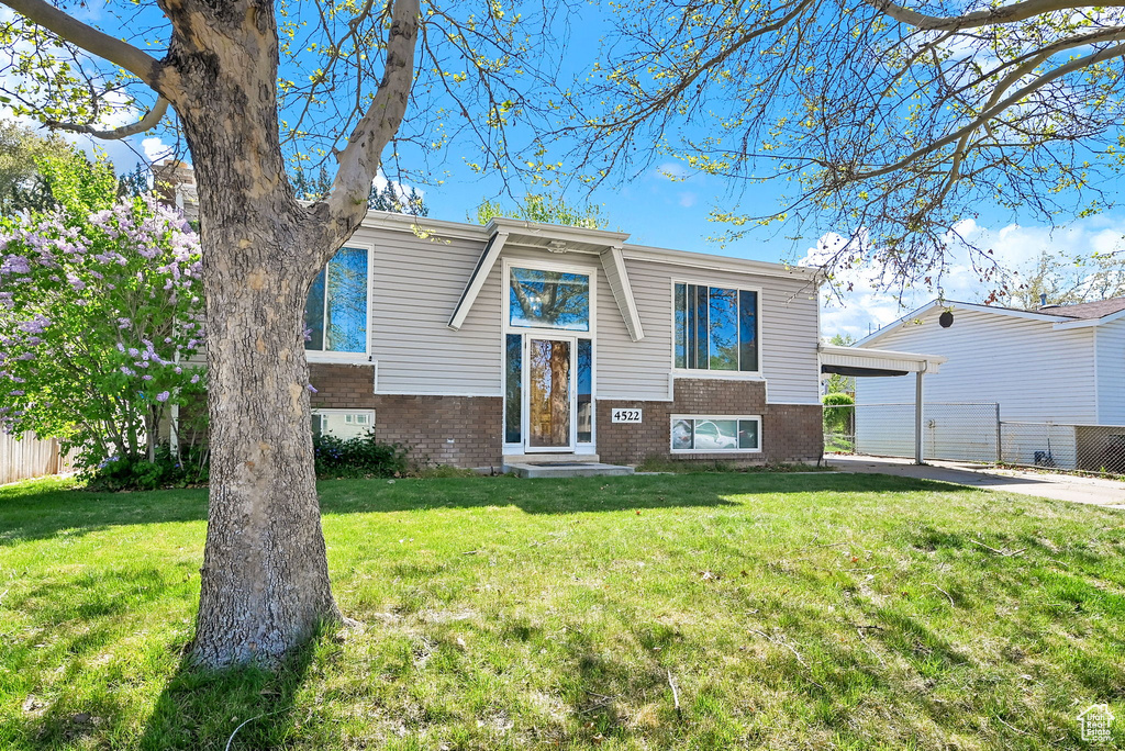 Split foyer home with brick siding, a front lawn, and fence