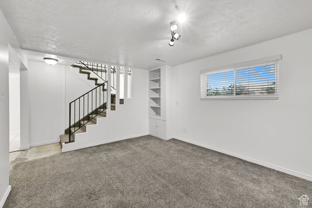 Interior space with a textured ceiling, carpet, baseboards, and stairway