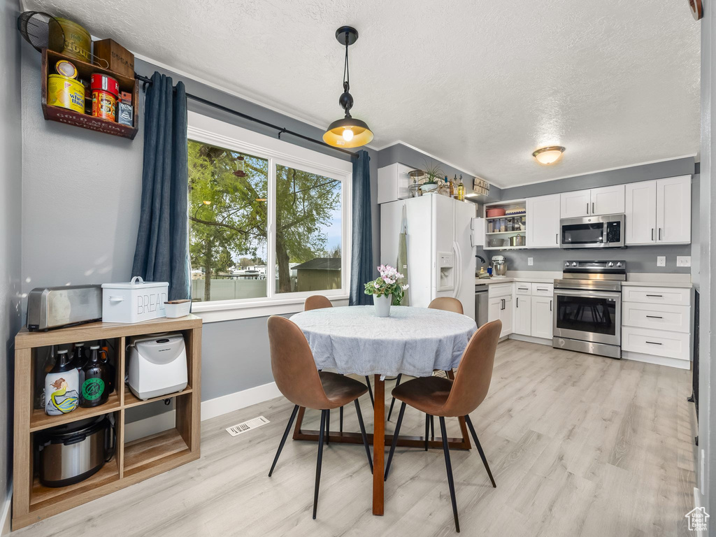 Dining space with baseboards, light wood-style flooring, a textured ceiling, and visible vents