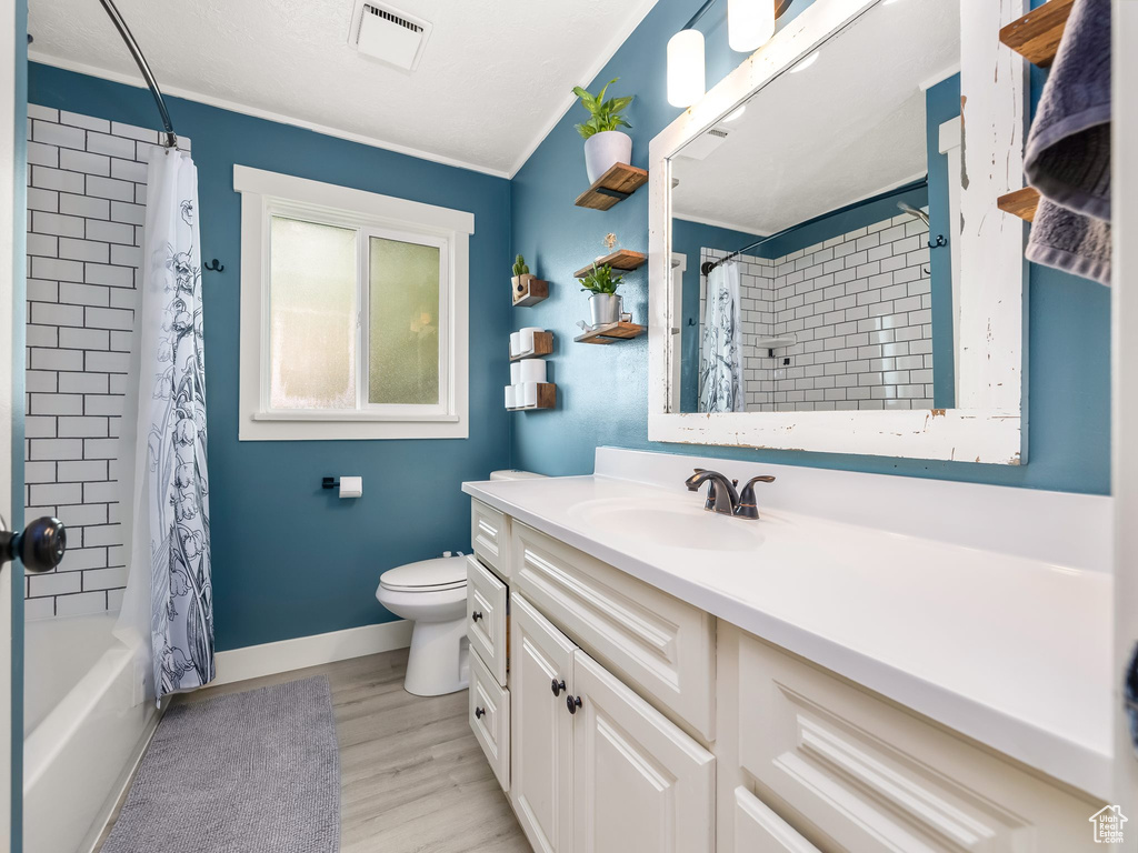 Bathroom featuring vanity, ornamental molding, shower / bath combo with shower curtain, wood finished floors, and toilet