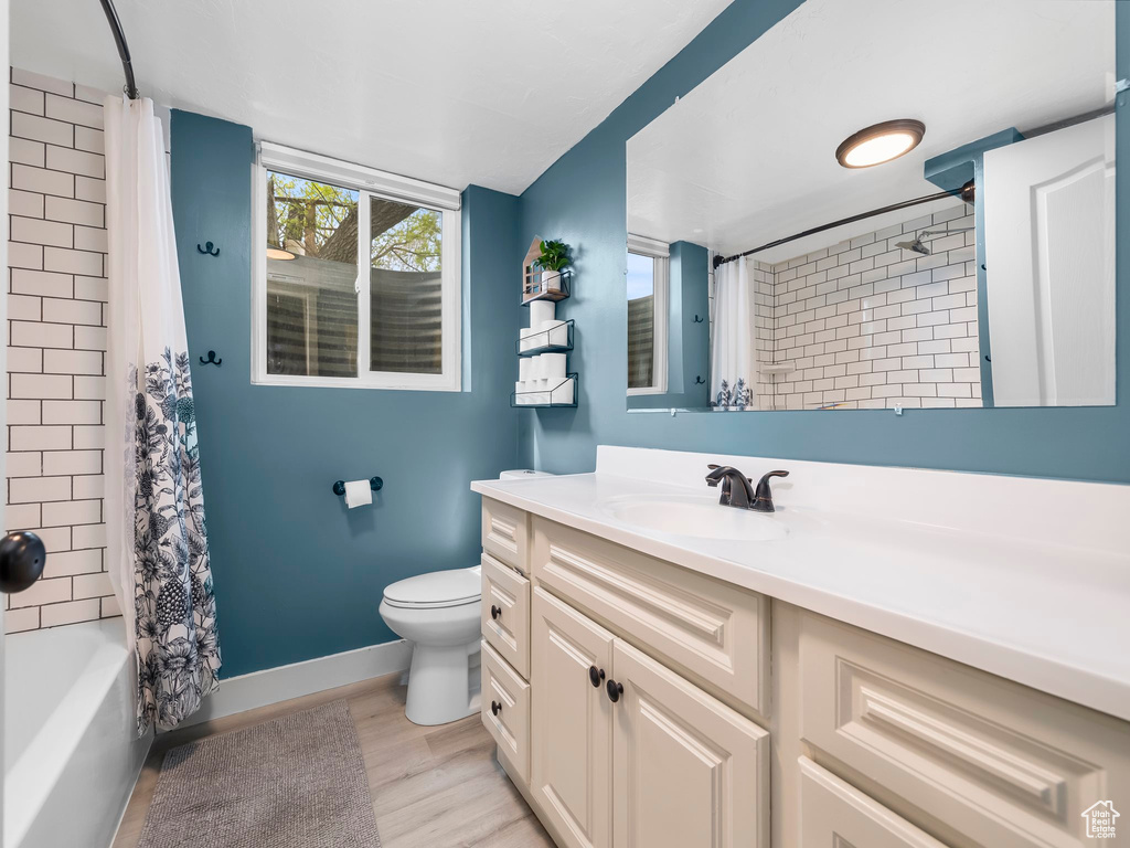 Bathroom featuring shower / bath combo with shower curtain, vanity, wood finished floors, toilet, and baseboards