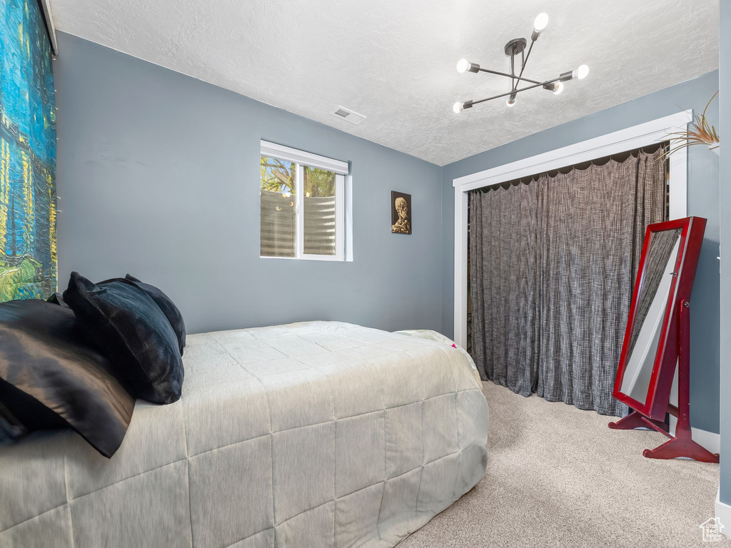 Bedroom with carpet floors, a textured ceiling, an inviting chandelier, and visible vents
