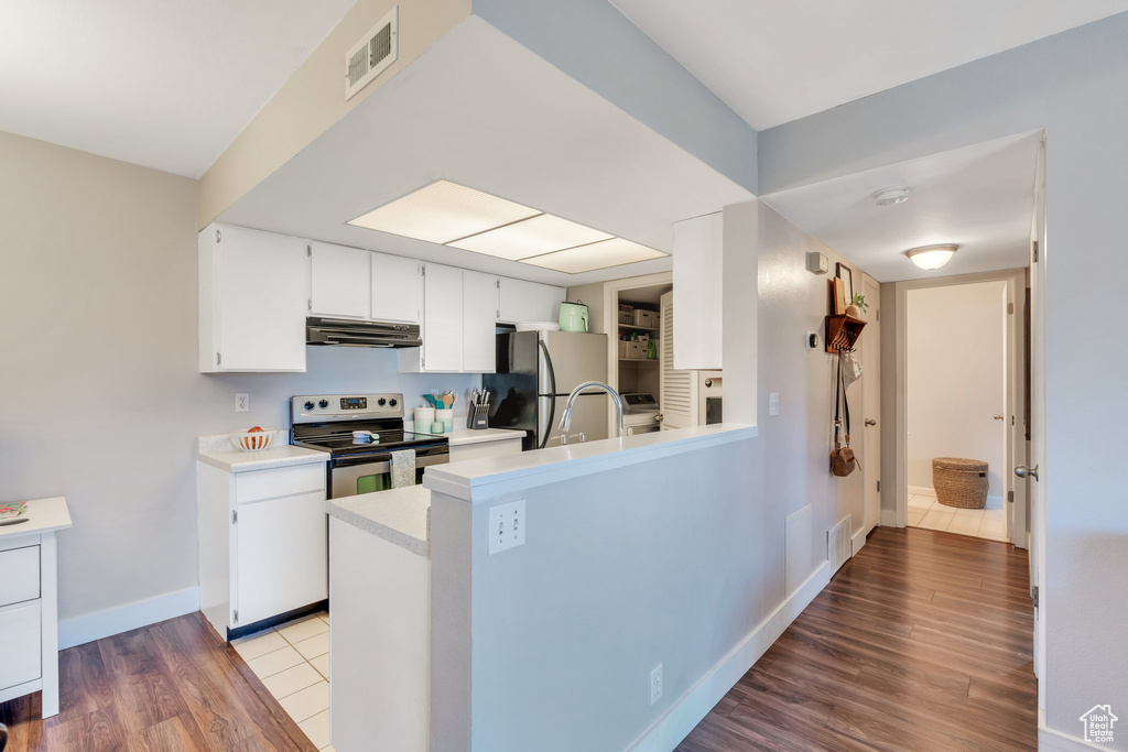 Kitchen with light countertops, stainless steel appliances, wood finished floors, under cabinet range hood, and visible vents