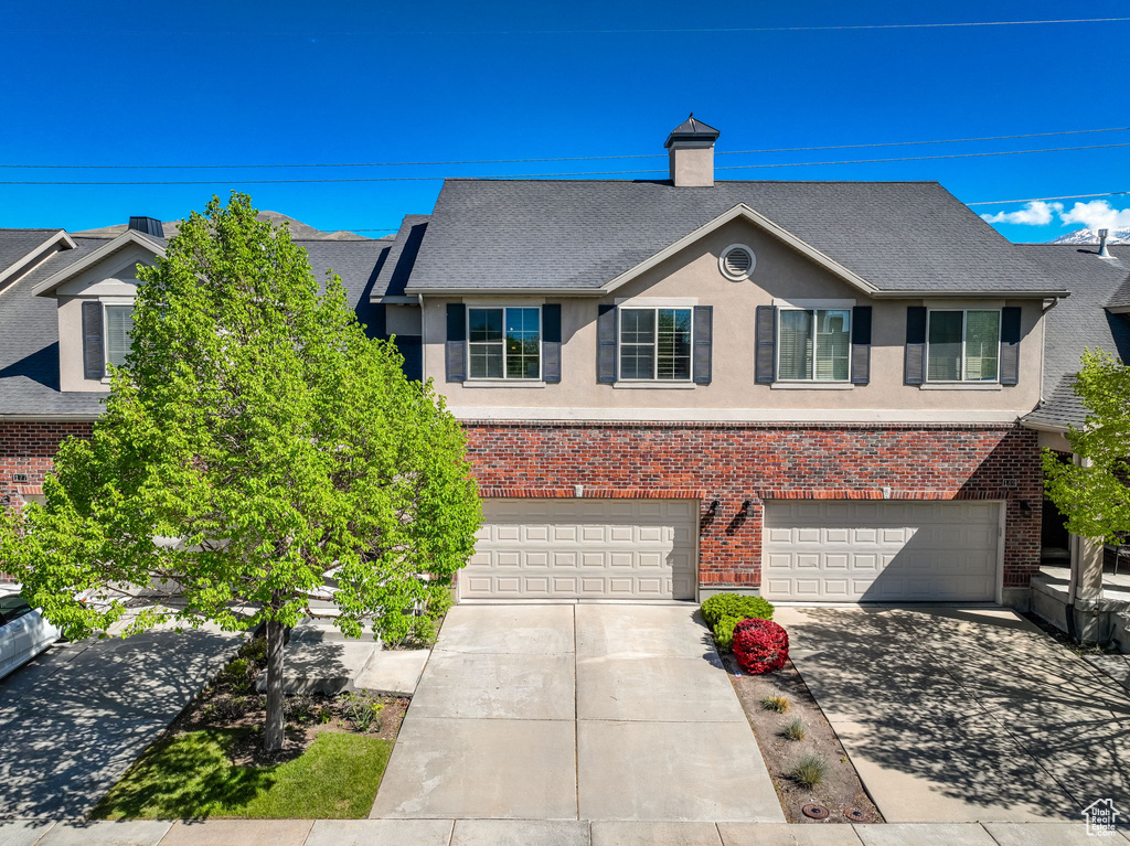 Multi unit property with driveway, roof with shingles, brick siding, an attached garage, and stucco siding