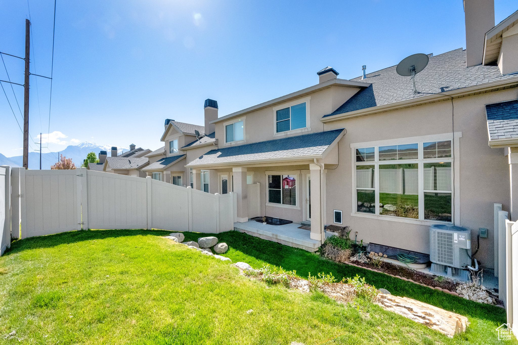 Back of property with fence, stucco siding, a chimney, cooling unit, and a lawn