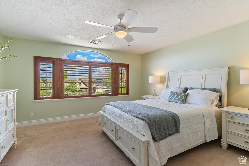 Bedroom featuring visible vents, baseboards, light colored carpet, a textured ceiling, and a ceiling fan